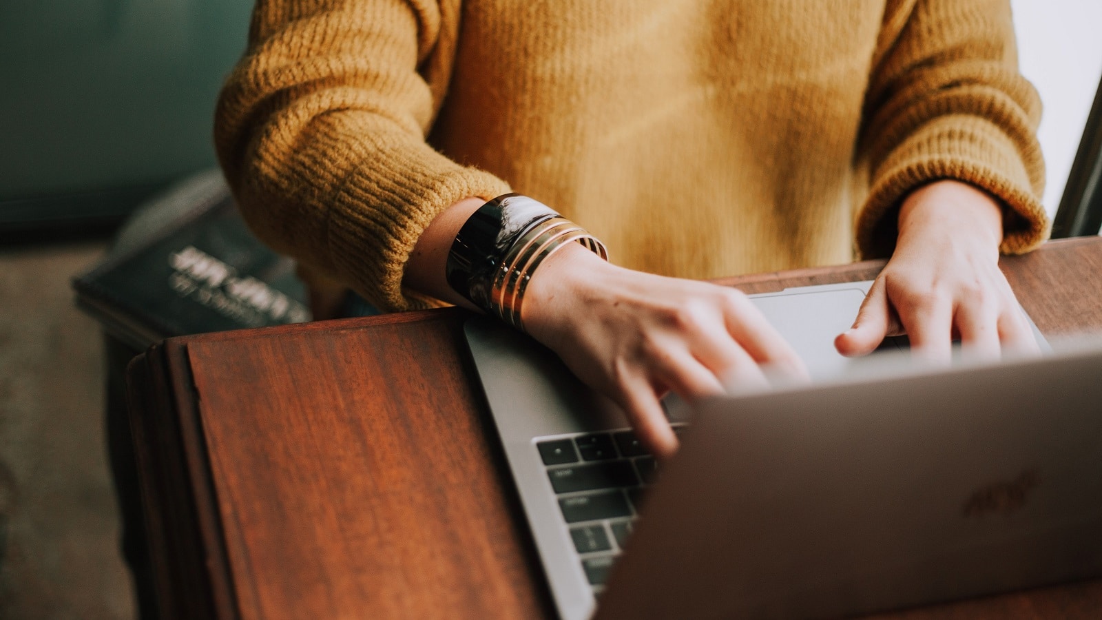 Woman in orange sweater and bracelt typing on laptop