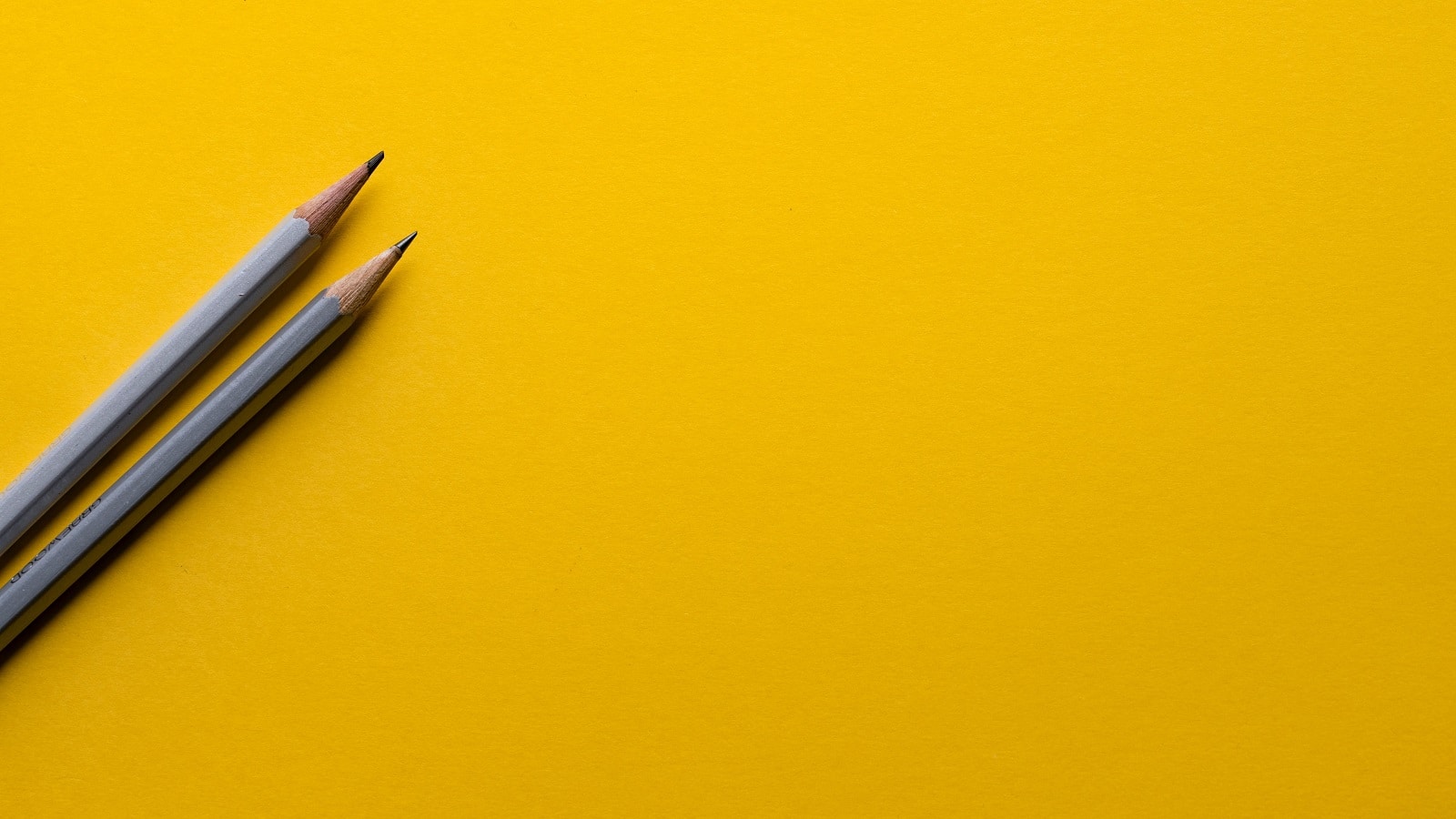 Two gray wooden pencils on yellow background