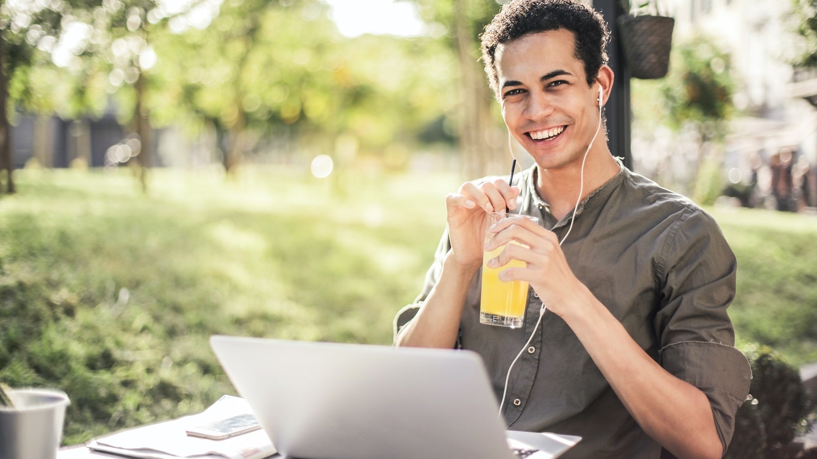 Man sipping orange drink in park in front of his laptop