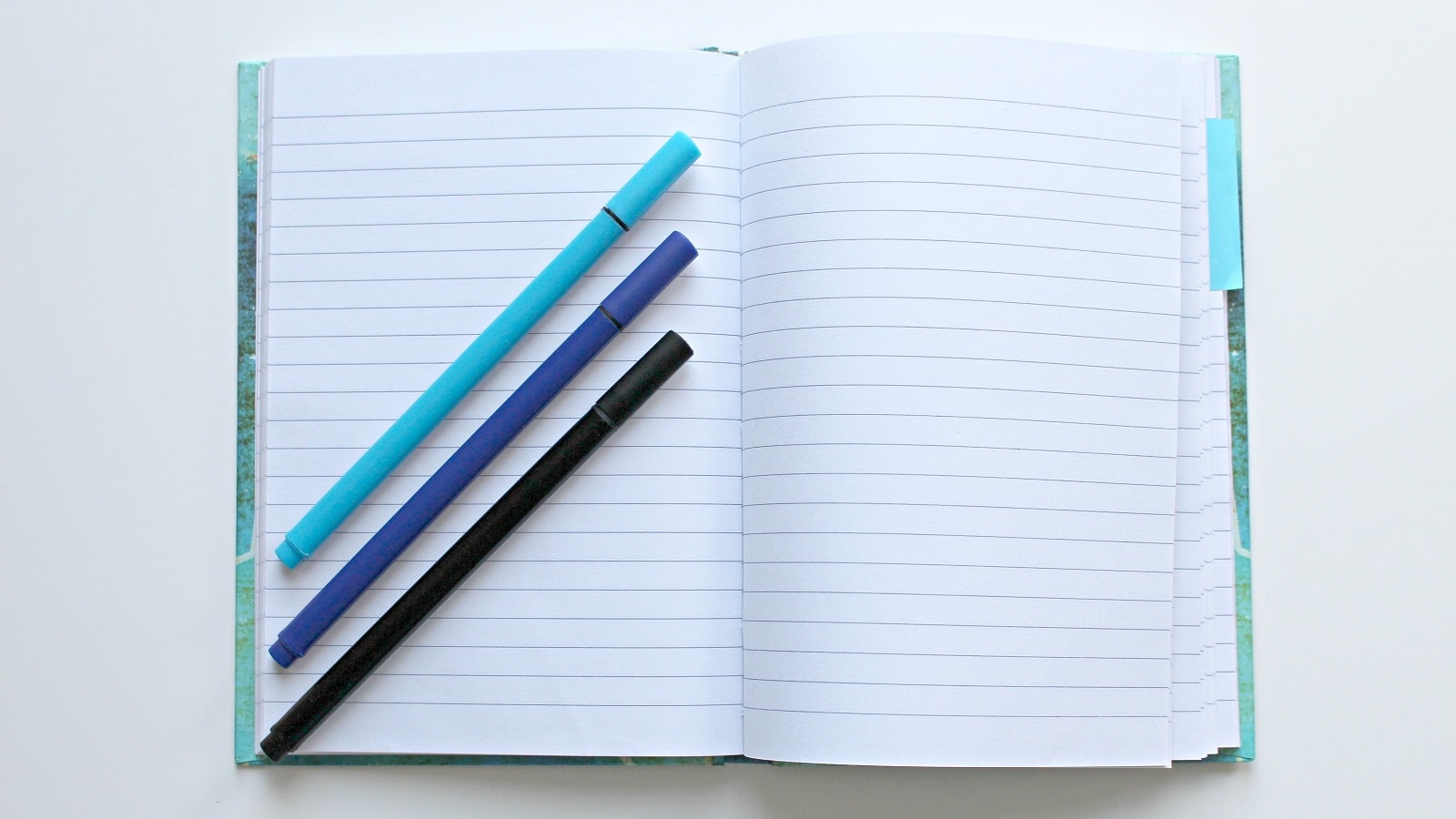 Blue empty notebook open with three blue pens
