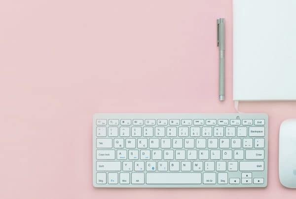 Wireless keyboard, wireless mouse, notebook and pen on a pink table
