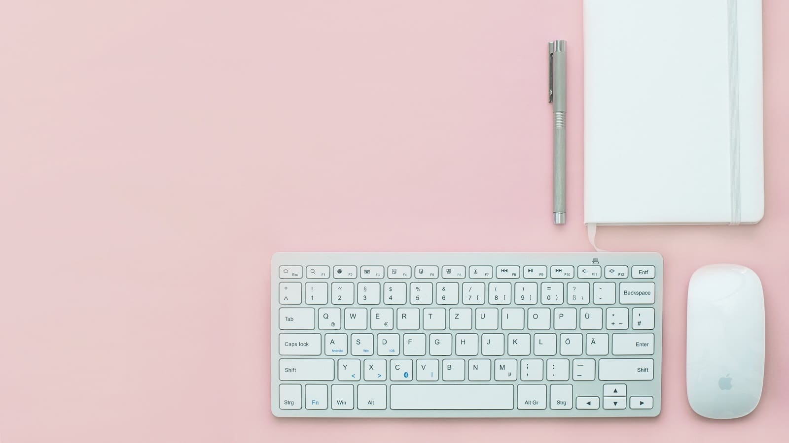 Wireless keyboard, wireless mouse, notebook and pen on a pink table