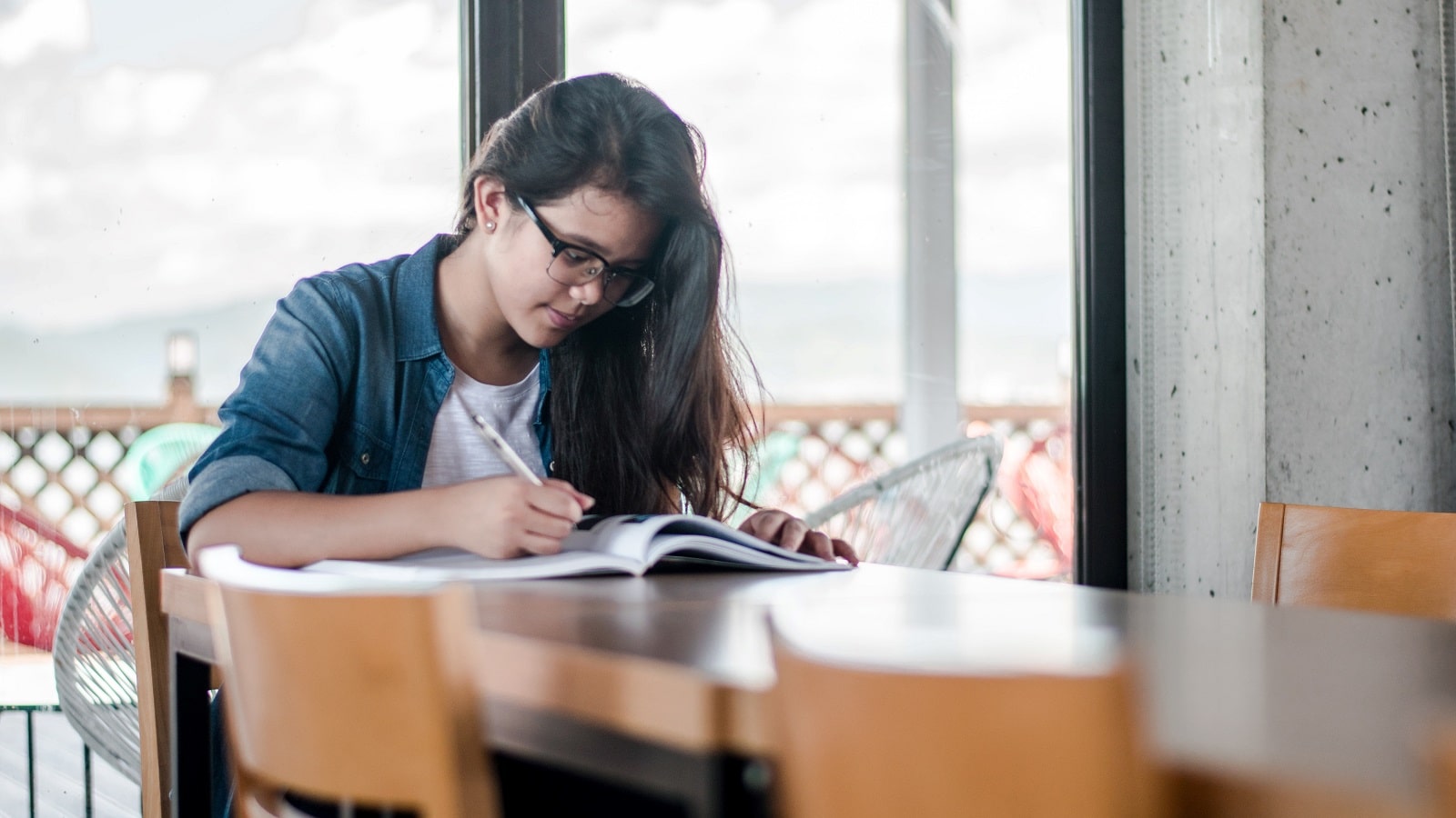 Student in glasses reading from a textbook on a wooden table