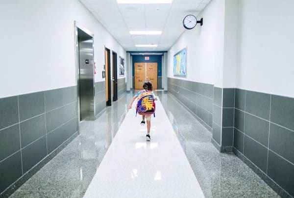 Child in backpack skipping down empty hallway