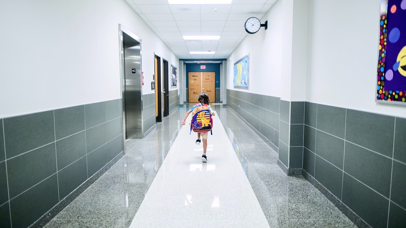 Child in backpack skipping down empty hallway