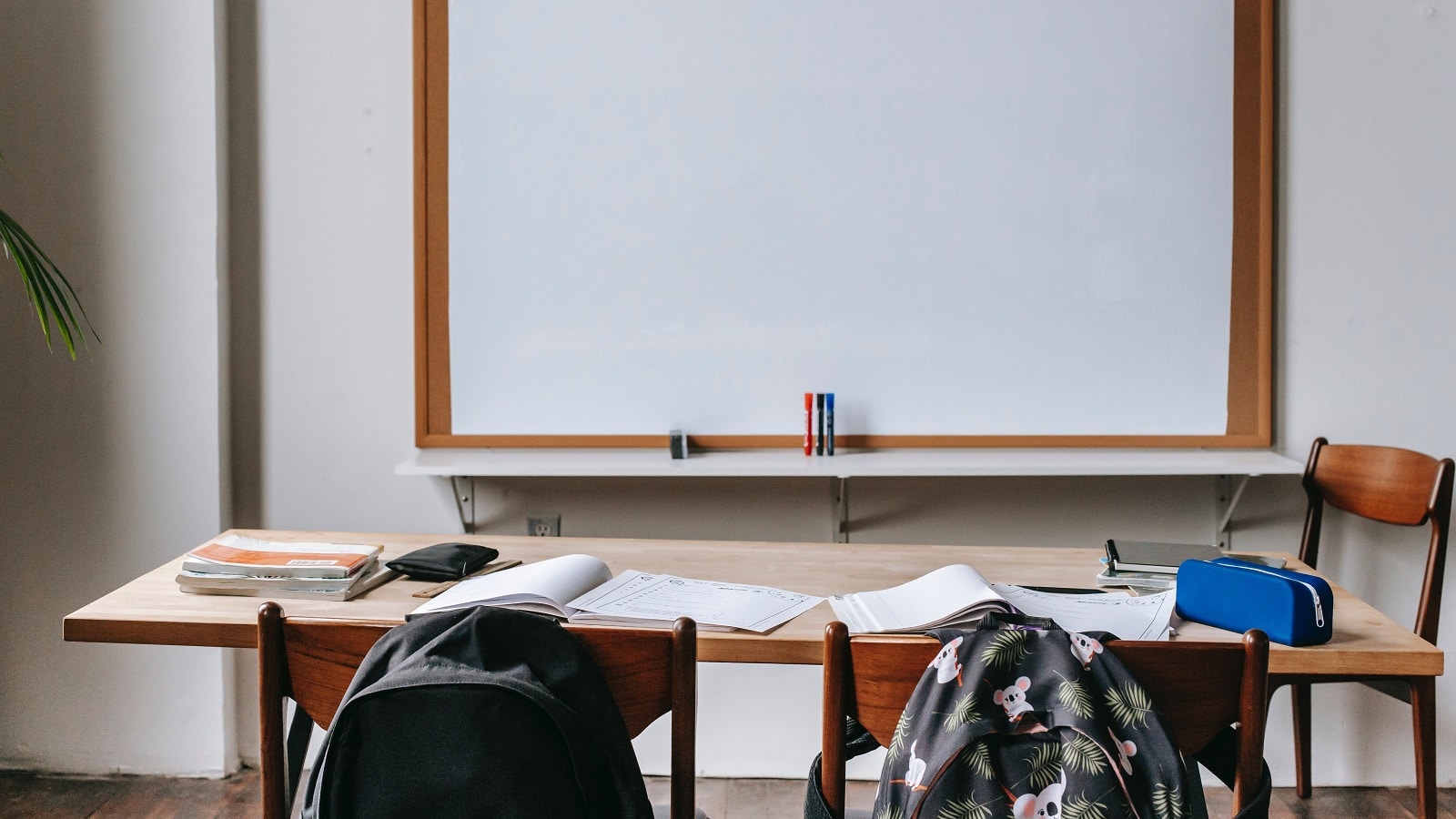 Blank whiteboard with student table in foreground, backpacks on backs of chairs