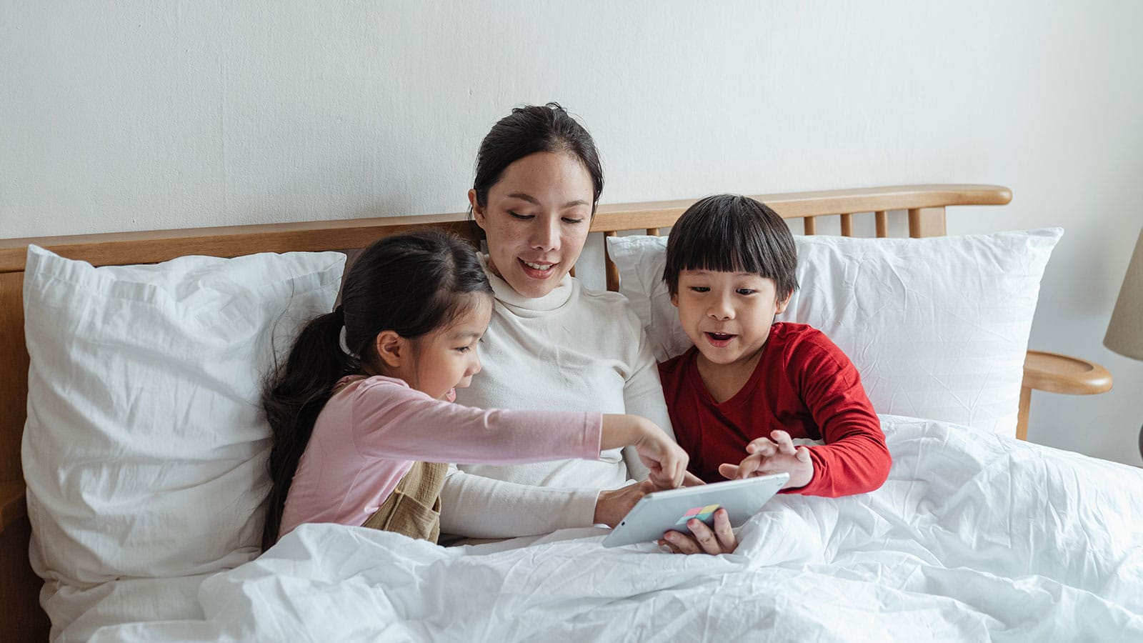 Woman and Kids Sitting on Bed While Using Tablet Computer