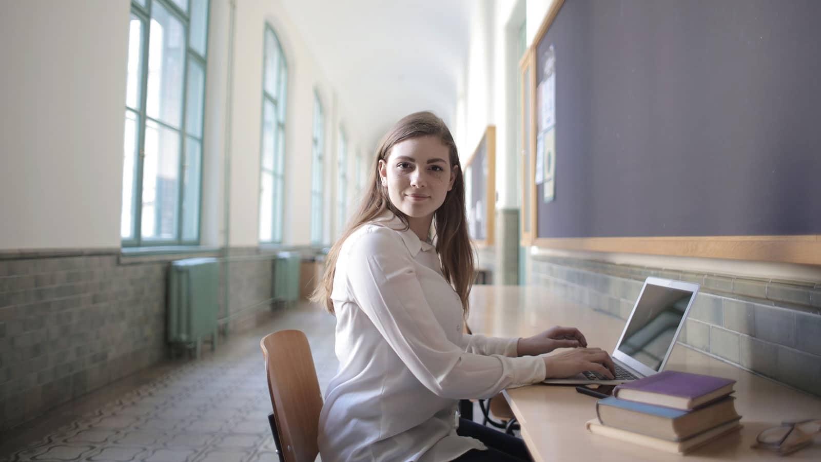 Female student typing on laptop in university hallway