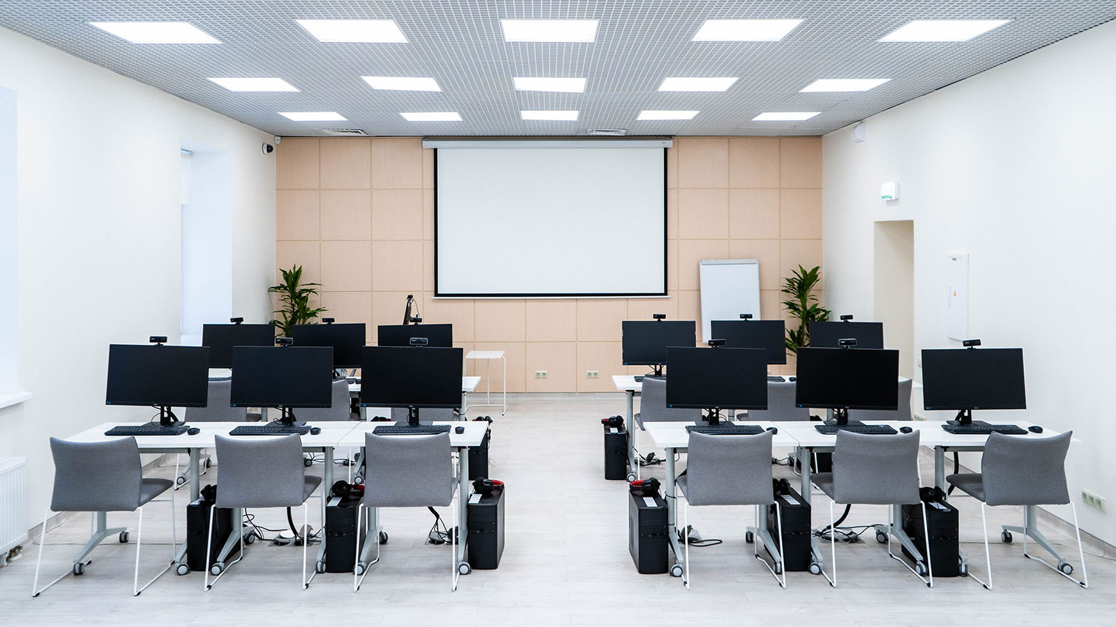 Presentation room with tables, chairs, monitors, and a large presentation screen