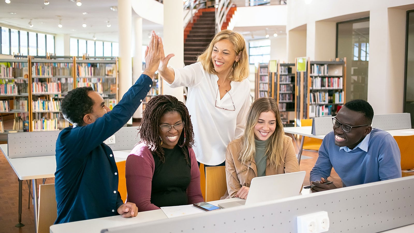 Cheerful multiethnic students having high five with teacher