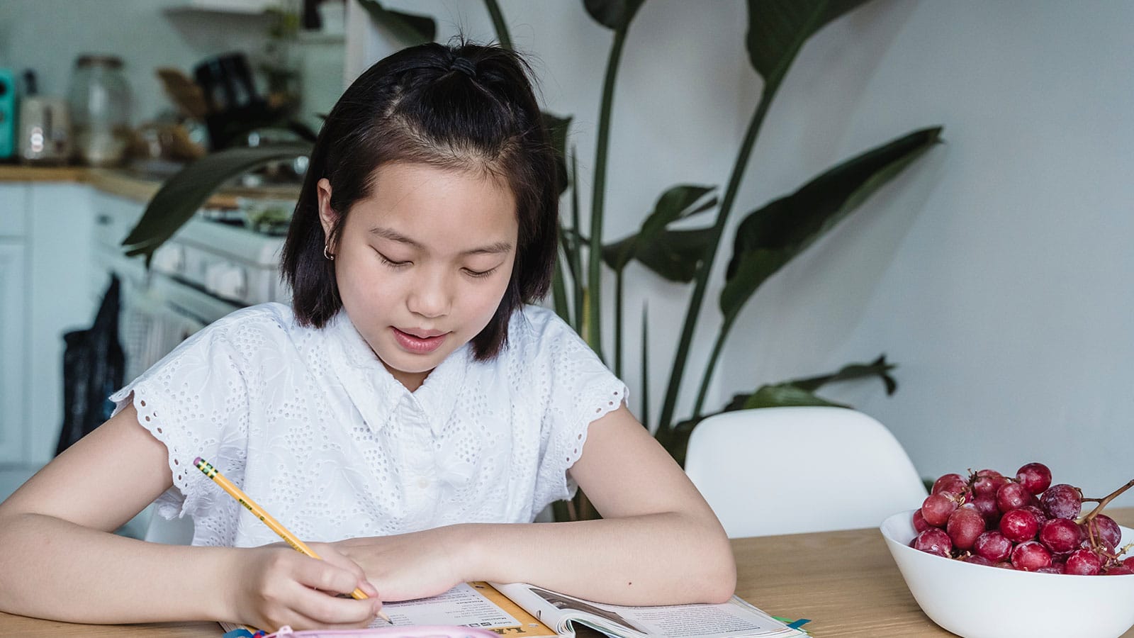 A Girl in White Top Writing on a Notebook