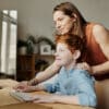 Mother leaning over her son while they look at a computer screen