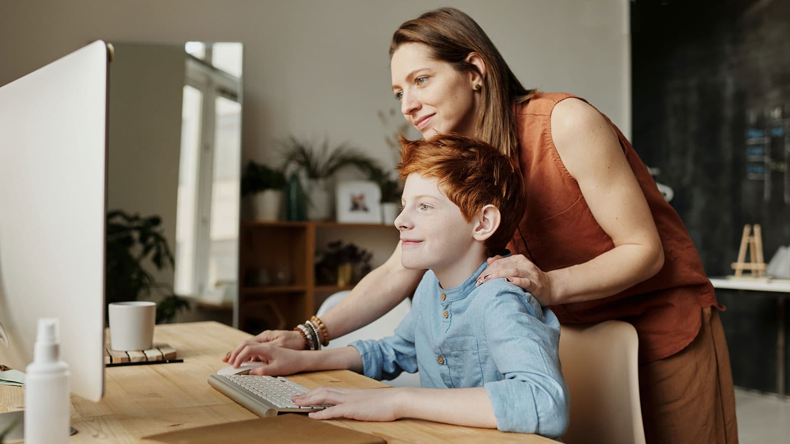 Mother leaning over her son while they look at a computer screen