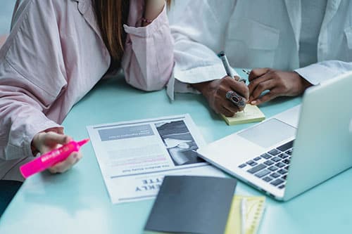 Two people making notes while looking at a laptop