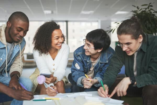 Four high school students sitting around a table working on a project smiling at each other
