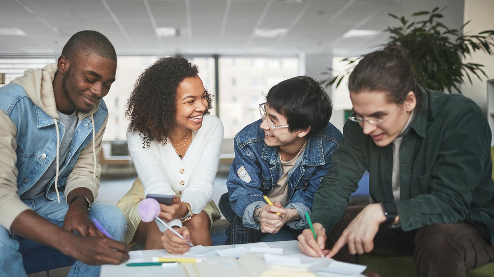 Four high school students sitting around a table working on a project smiling at each other