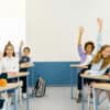 Classroom full of students raising their hands to answer a question