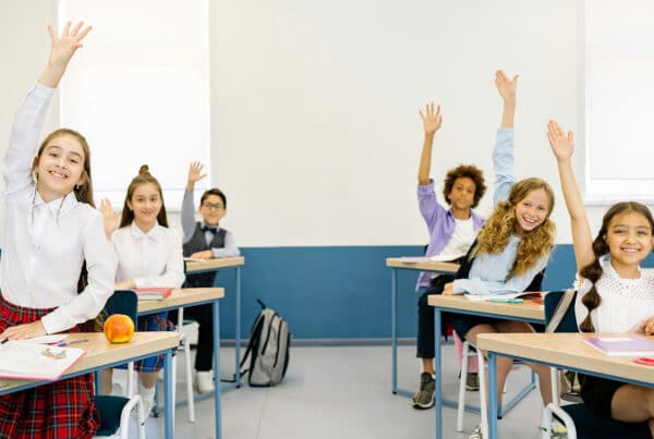 Classroom full of students raising their hands to answer a question