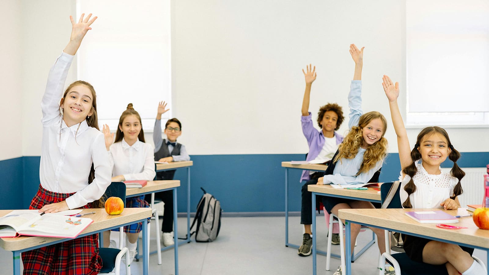 Classroom full of students raising their hands to answer a question
