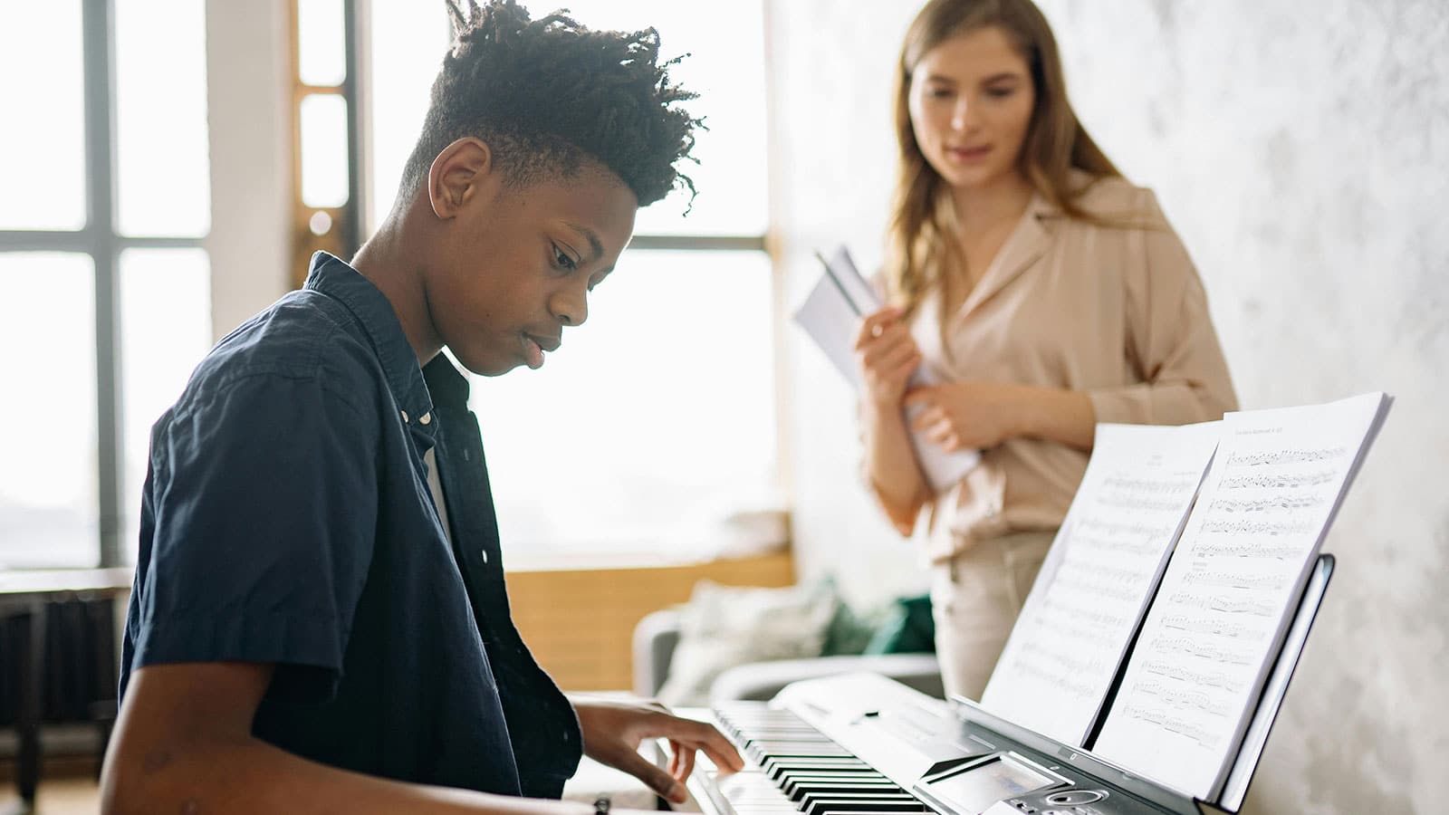 Young adult student playing the piano with a tutor watching