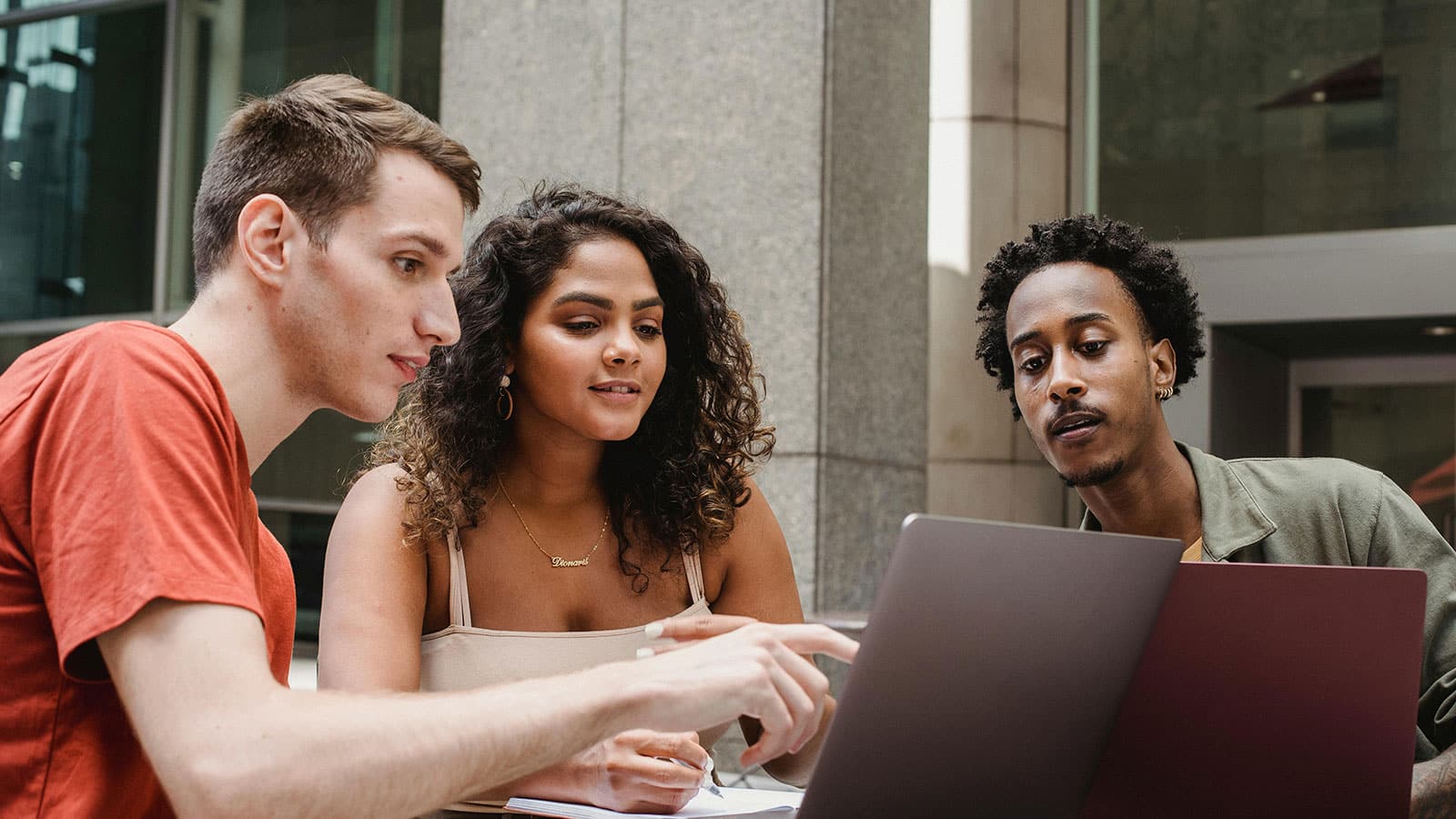 Three students sitting at a table with two laptops studying