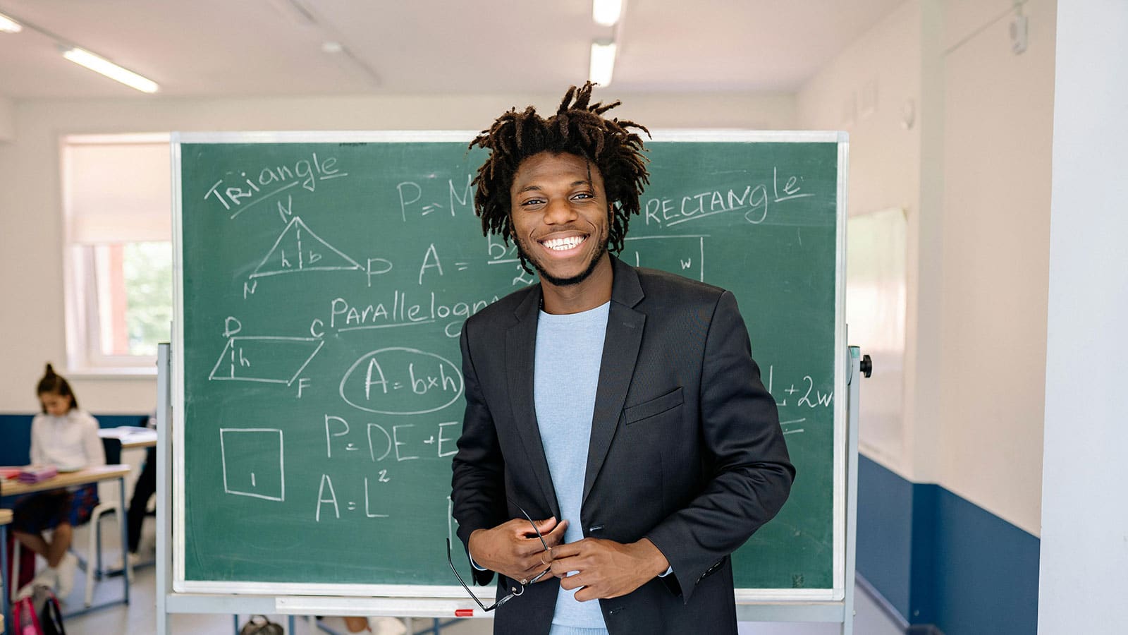 Student standing in front of a green chalkboard smiling