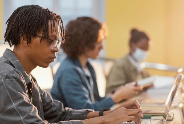 Student typing at a laptop with two students in the background typing as well at a table
