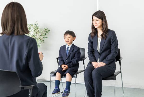 Mother and child dressed up sitting in chairs in front of a woman interviewing them