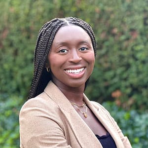 A smiling student in a light brown dress suit with an outdoor background