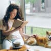 Female student reading a book on a window ledge while petting her dog