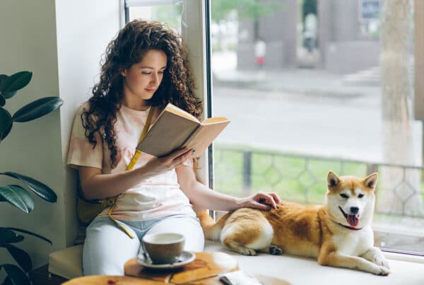 Female student reading a book on a window ledge while petting her dog