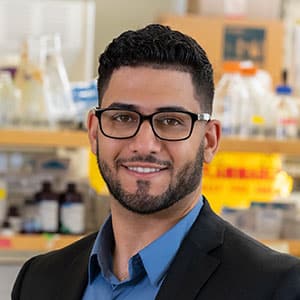 Scholarship winner Yahia Abuhasan in glasses and a suite standing in front of a laboratory