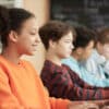 Image of a row of teens in a classroom looking at screens with one girl smiling near the front