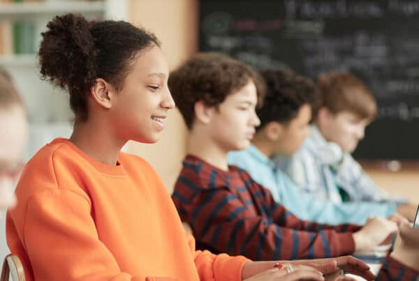 Image of a row of teens in a classroom looking at screens with one girl smiling near the front