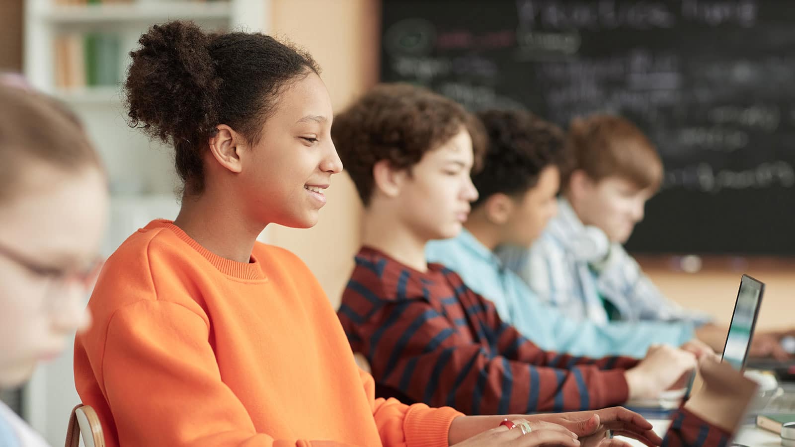 Image of a row of teens in a classroom looking at screens with one girl smiling near the front
