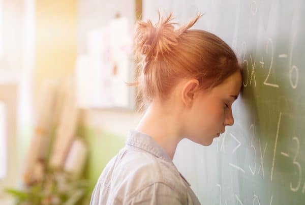 Image of an anxious student with forehead resting on a chalkboard with math equations
