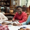 Image of several college students sitting at a table in a library smiling with open books in front of them as they study