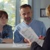 Image of a father and daughter sitting behind a desk with a back view of a woman looking over paperwork