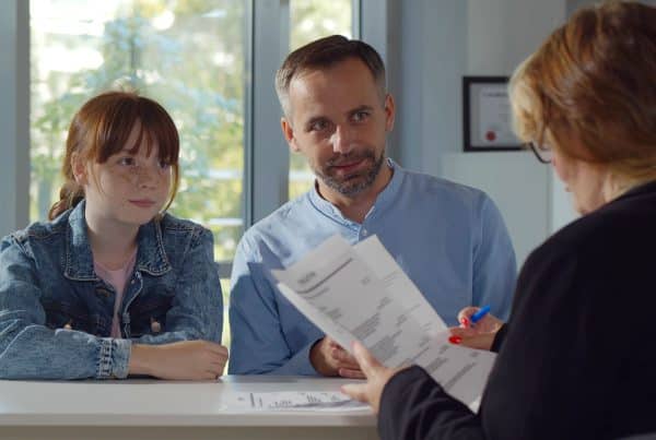 Image of a father and daughter sitting behind a desk with a back view of a woman looking over paperwork