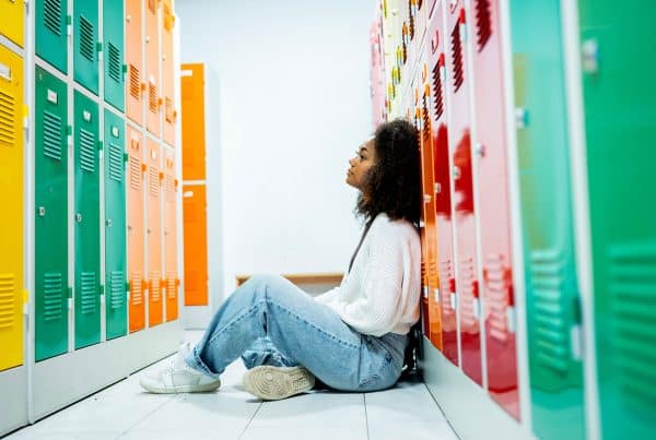Teen girl sitting alone on the floor by school lockers feeling stressed