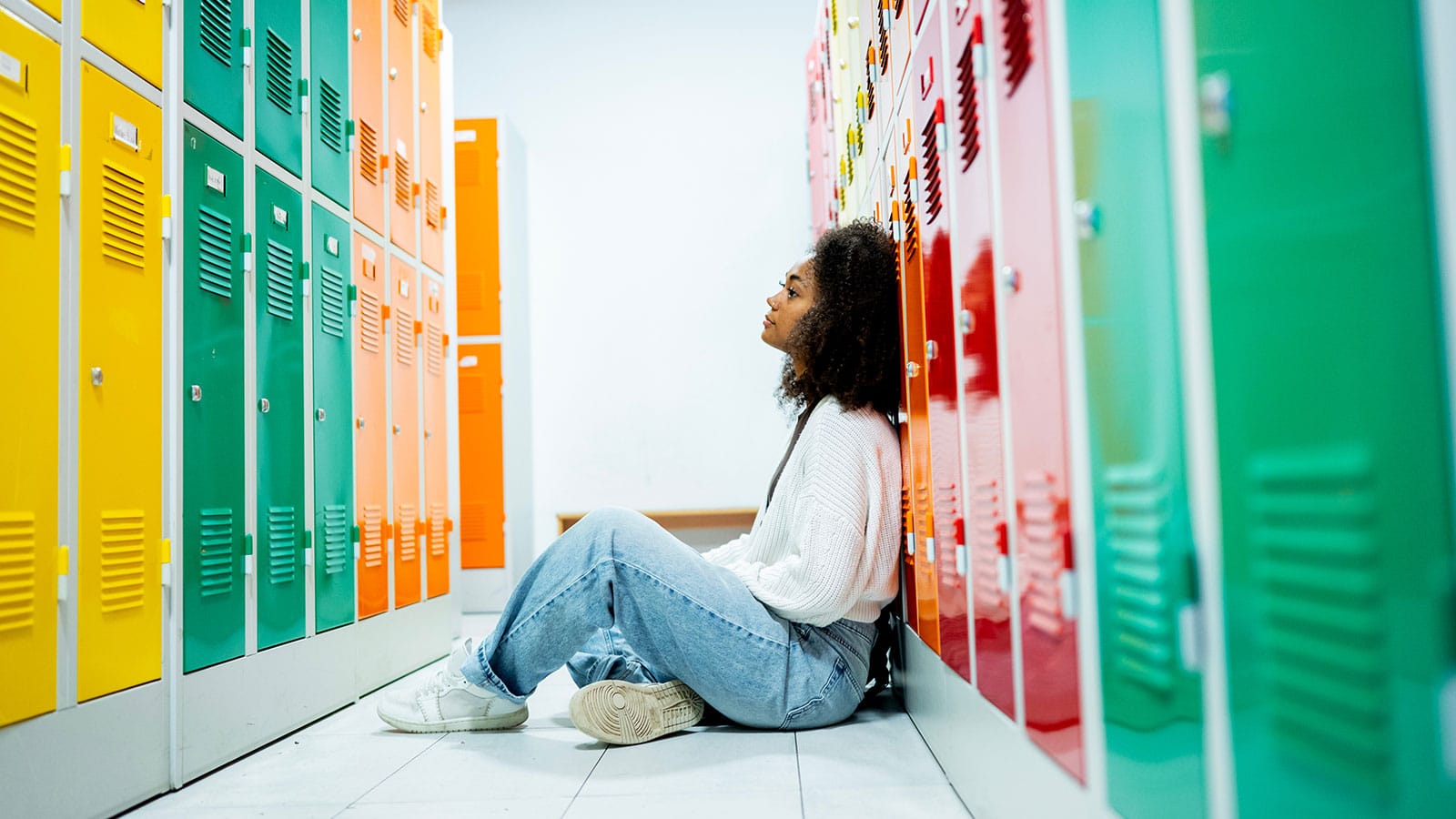 Teen girl sitting alone on the floor by school lockers feeling stressed