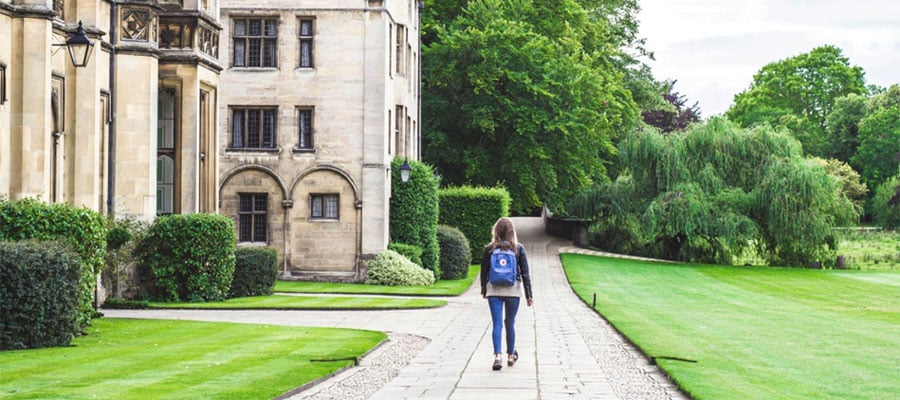 A view of the back of a student as they walk down a sidewalk with a college building beside them