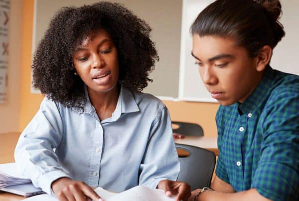 An instructor next to a student with her hand on a desk showing the student something on a page